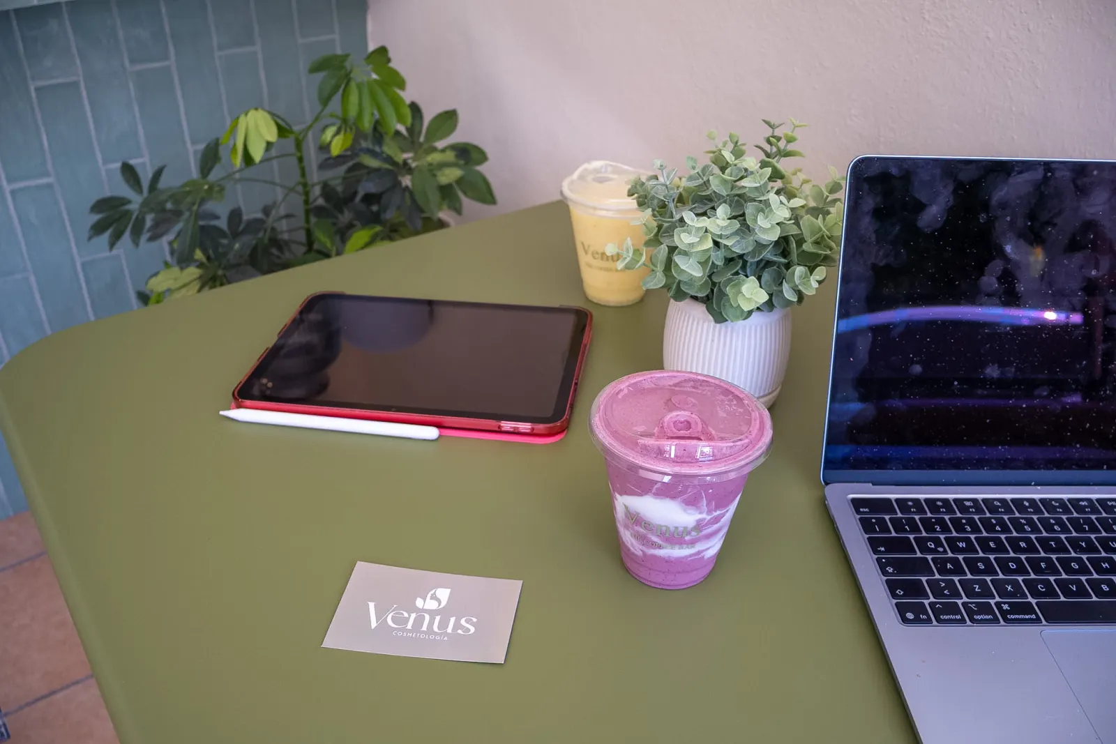 Mesa de trabajo verde con bebidas Venus, tablet y laptop